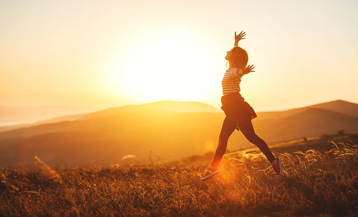 A happy and energetic woman is jumping at sunset in the mountains